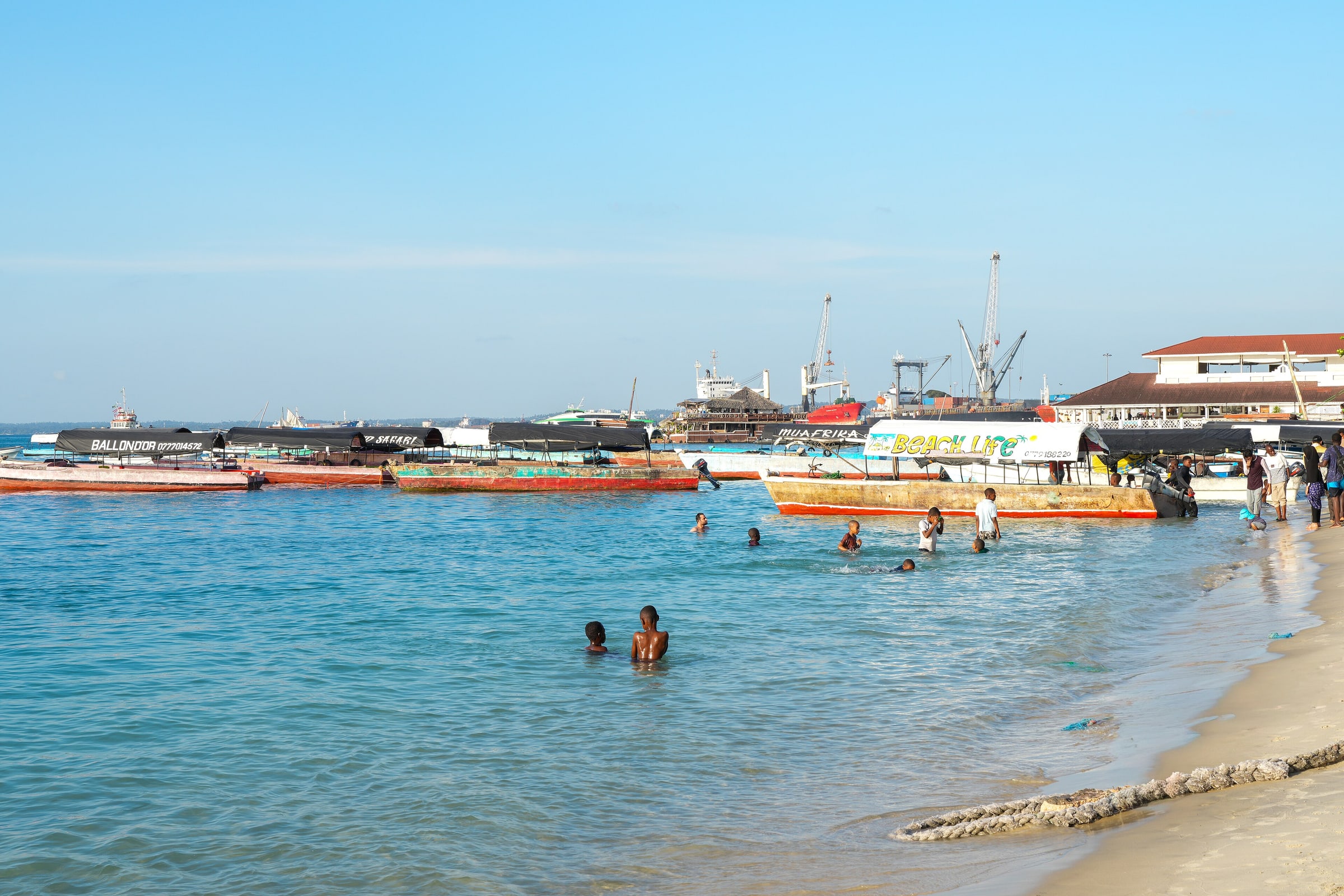 Beach with boats and people swimming, Stone Town harbour, Zanzibar